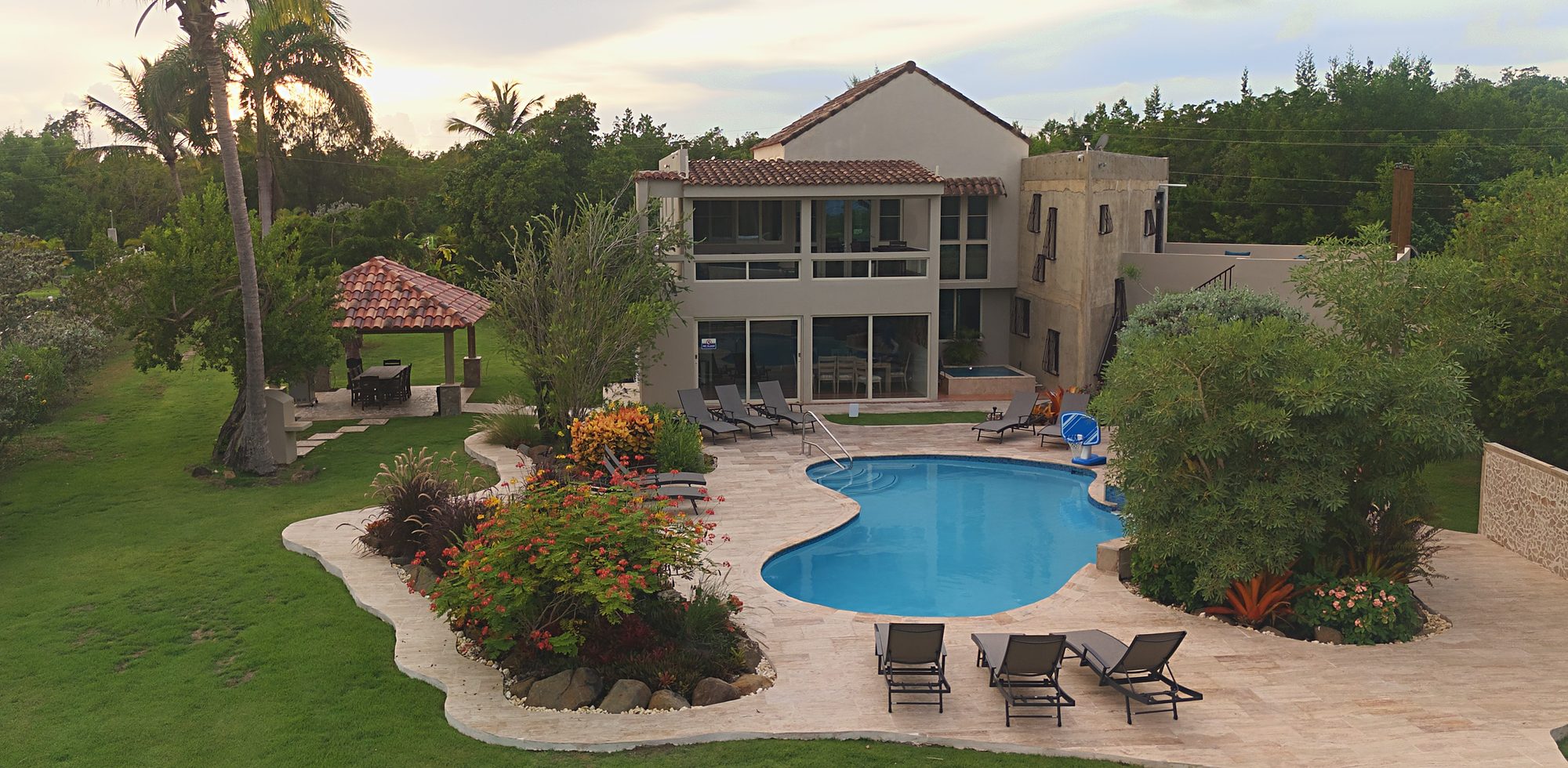 The Nice Beach Oasis: two-story Caribbean home with a free-form pool, travertine deck and tropical gardens in Río Grande, Puerto Rico, in warm afternoon light